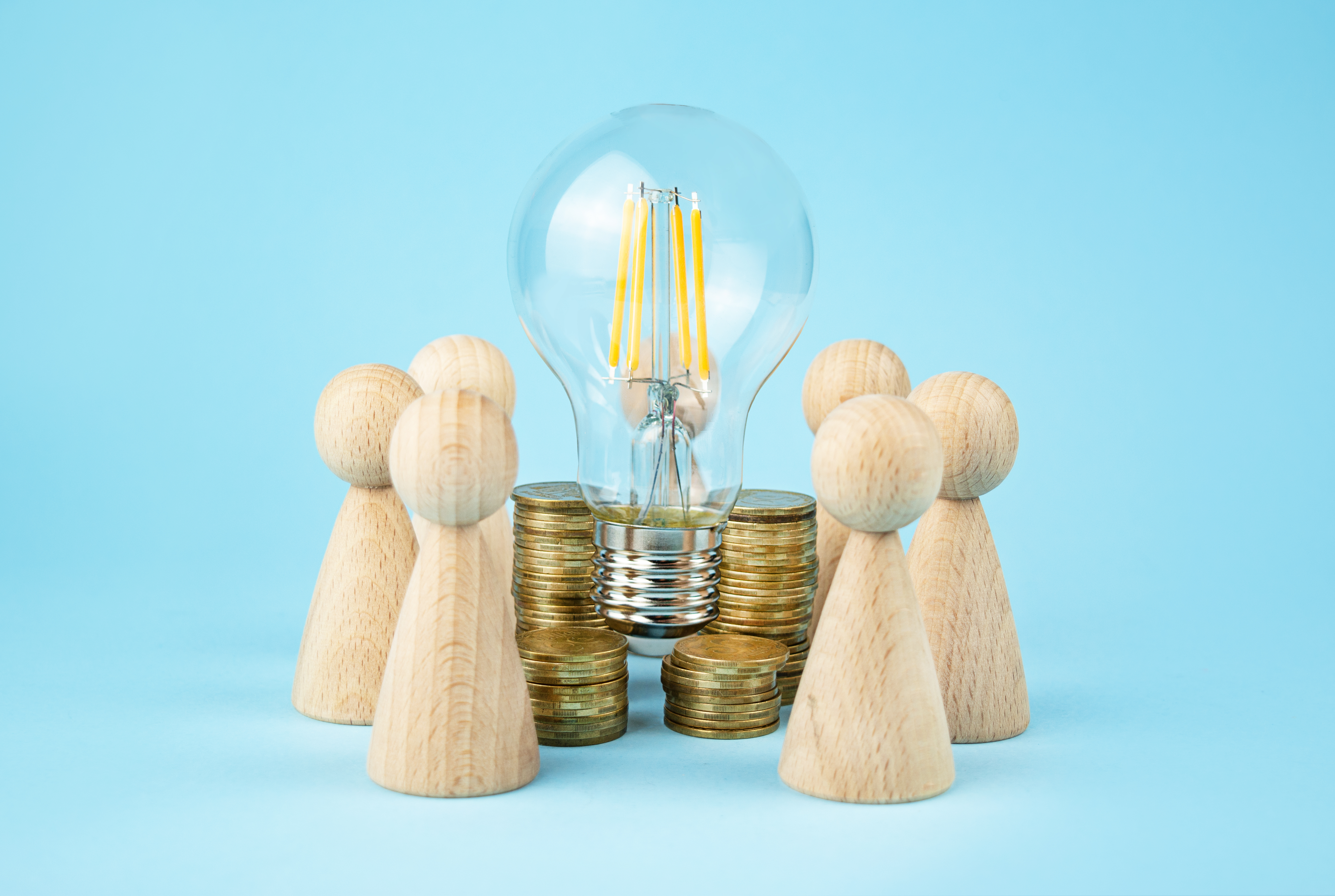 Business concept. Team concept and idea generation. Wooden figures of people stand around coins and a lamp on a blue background. Team work. Copy space.